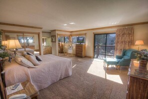 A spacious hotel room with a large bed, a sitting area with a chair, a desk, and a balcony with a view. - Tkh1226 - Emerald Lodge 6 Bedroom Home (South Lake Tahoe)