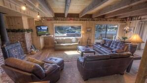 A cozy living room with a fireplace, leather sofas, a television, and a large window with a view of the street. - Tkh1226 - Emerald Lodge 6 Bedroom Home (South Lake Tahoe)