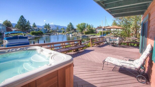 A wooden deck with a hot tub, lounge chairs, and a view of a marina with boats and mountains in the background. - Tkh1226 - Emerald Lodge 6 Bedroom Home (South Lake Tahoe)