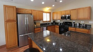 A modern kitchen with wooden cabinets, stainless steel appliances, granite countertops, and recessed ceiling lights.