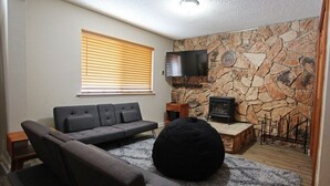 A living room with a stone wall, a fireplace, a television, and a black bean bag.