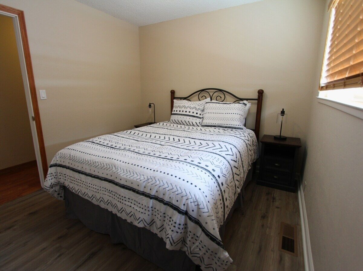 A bedroom with a bed, a nightstand, and a window with blinds.