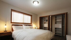 A bedroom with a bed, bedside lamps, a window with blinds, and a walk-in closet.