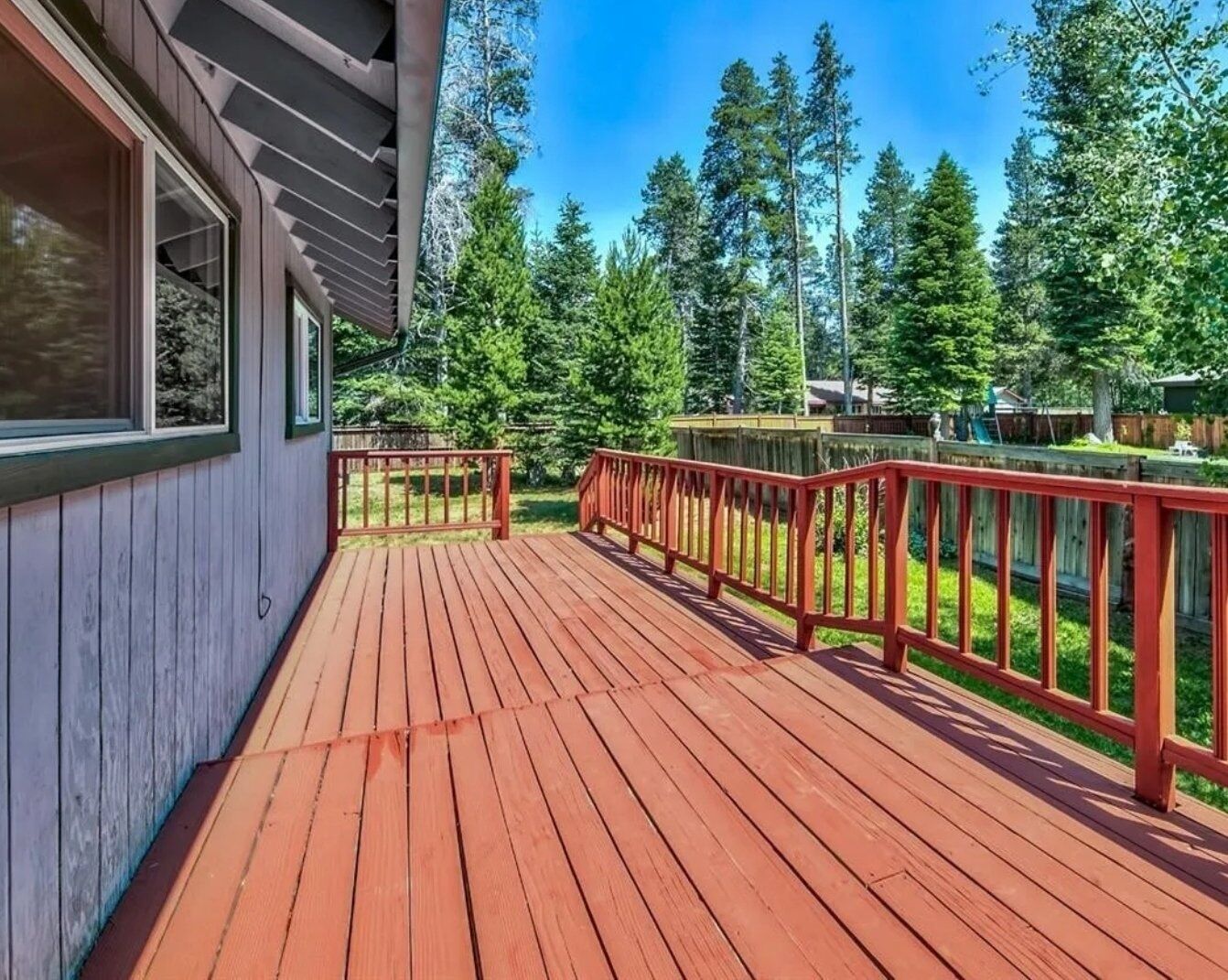 A wooden deck with red railings, surrounded by a forested area.