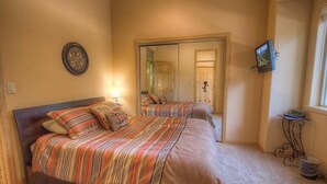 A bedroom with two beds, a mirror, a clock, and a television on the wall. - Coh1669 - Hawk's View Hideaway 6 Bedroom Home (South Lake Tahoe)
