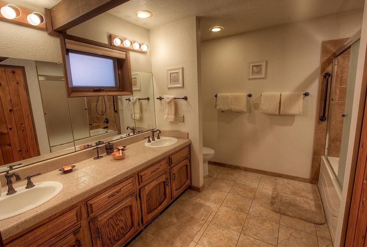 Une salle de bain avec deux lavabos, un grand miroir, un téléviseur placé au-dessus du miroir et un espace douche.