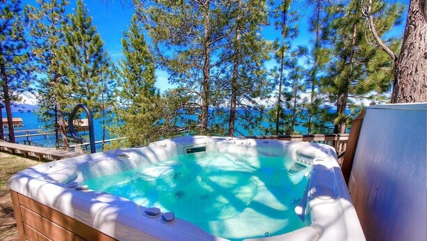 Un bain à remous avec une structure extérieure en bois, entouré d’arbres et surplombé d’un ciel bleu clair.