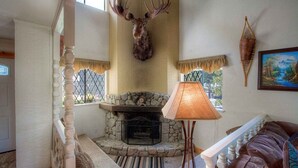 Une pièce chaleureuse avec une cheminée en pierre, une tête de cerf accrochée au mur et un coin salon confortable avec des coussins.