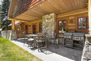 Eine Terrasse im Freien mit Steinpfeilern, einem Grill und Metallstühlen.
