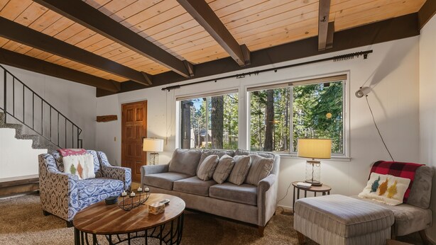 A cozy living room with a sofa, armchair, ottoman, and coffee table. A staircase with a wooden railing is visible in the background. - Coh0885 - Skyline Divine 4 Bedroom Home (South Lake Tahoe)