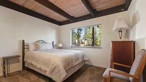A bedroom with a bed, a chair, a lamp, a window, and a wooden cabinet. - Coh0885 - Skyline Divine 4 Bedroom Home (South Lake Tahoe)