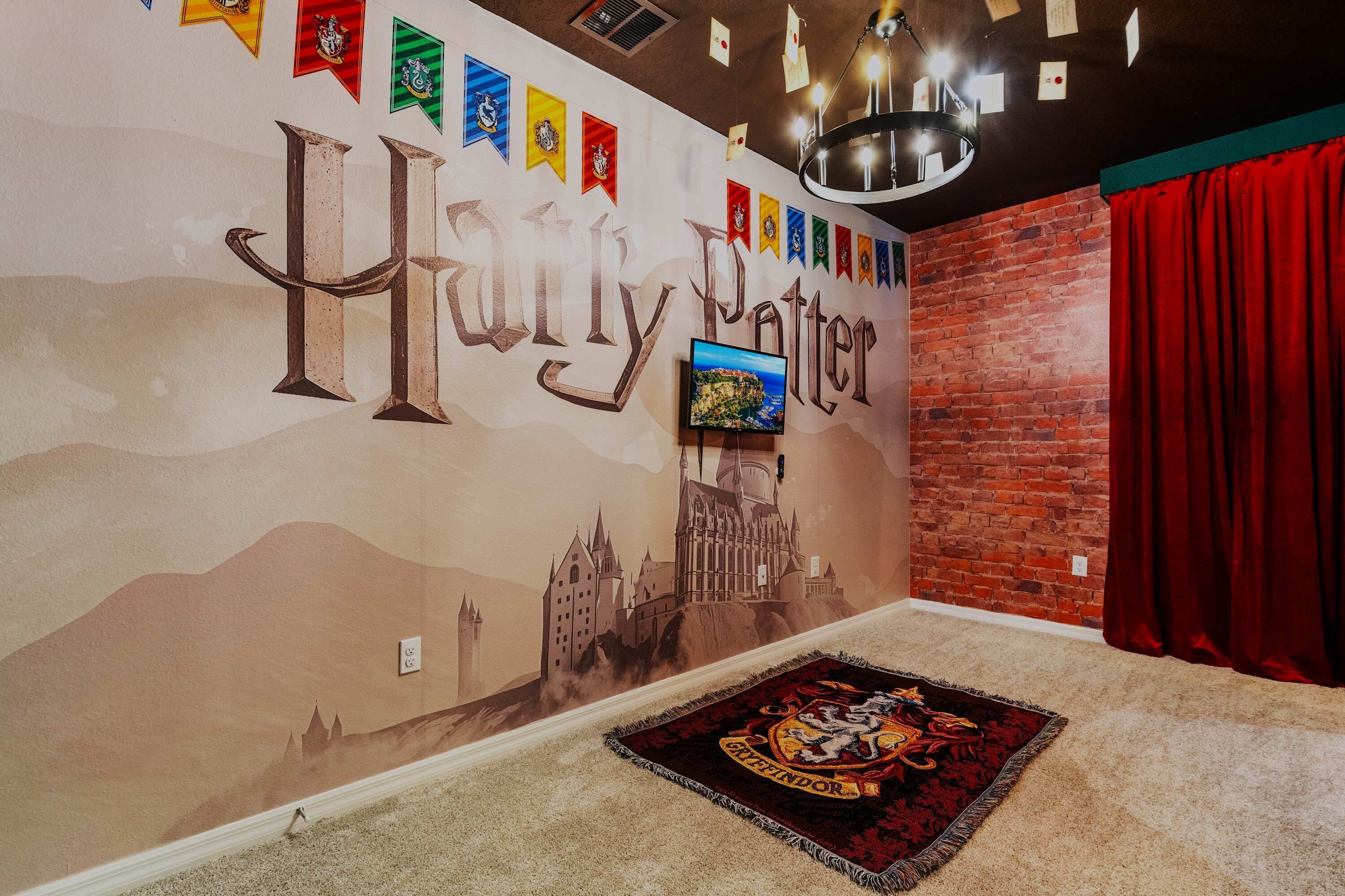 A room with a Harry Potter themed wall mural, a flat-screen TV, and a Hogwarts carpet.
