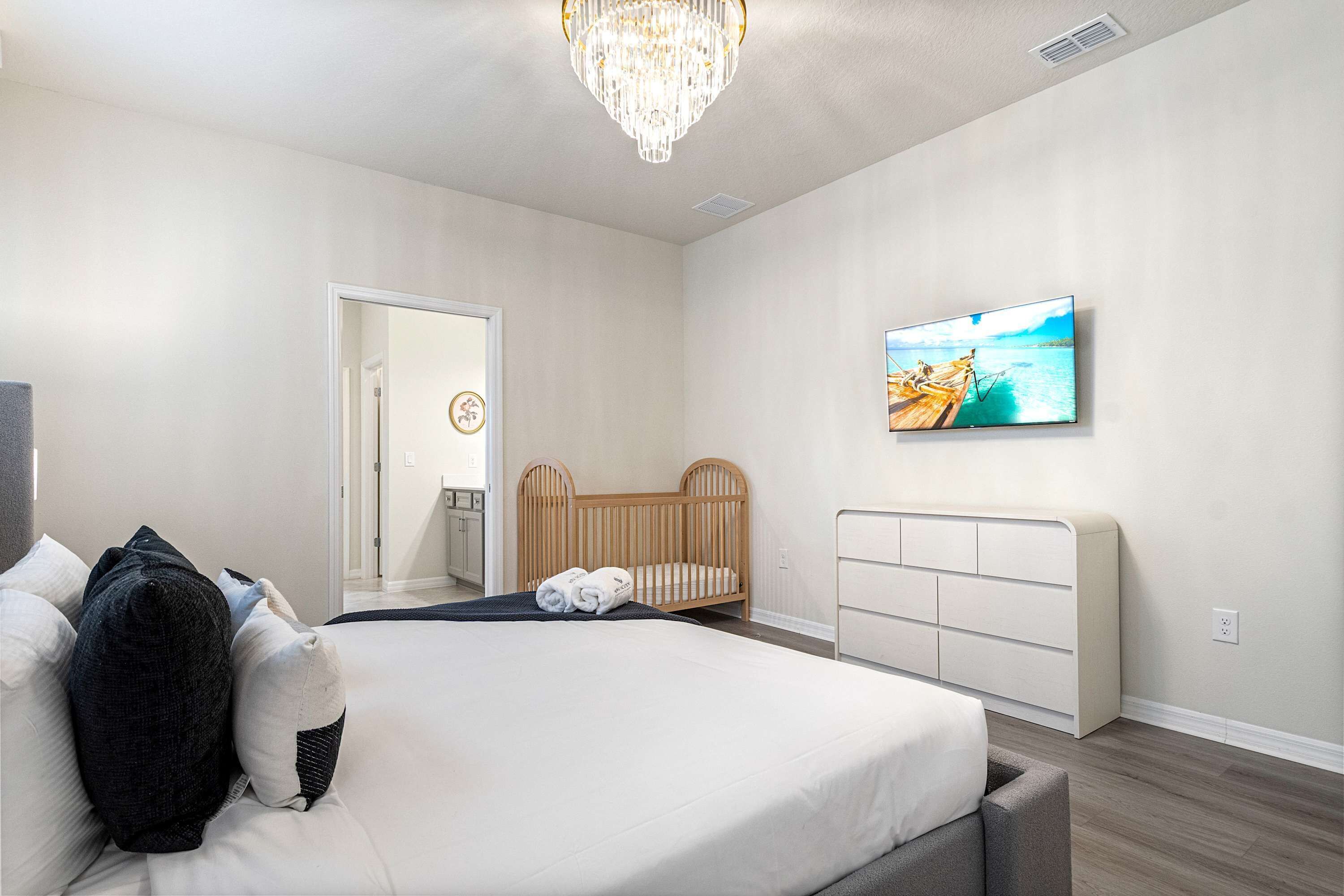 A modern bedroom with a large bed, a wooden crib, a television, and a chandelier.