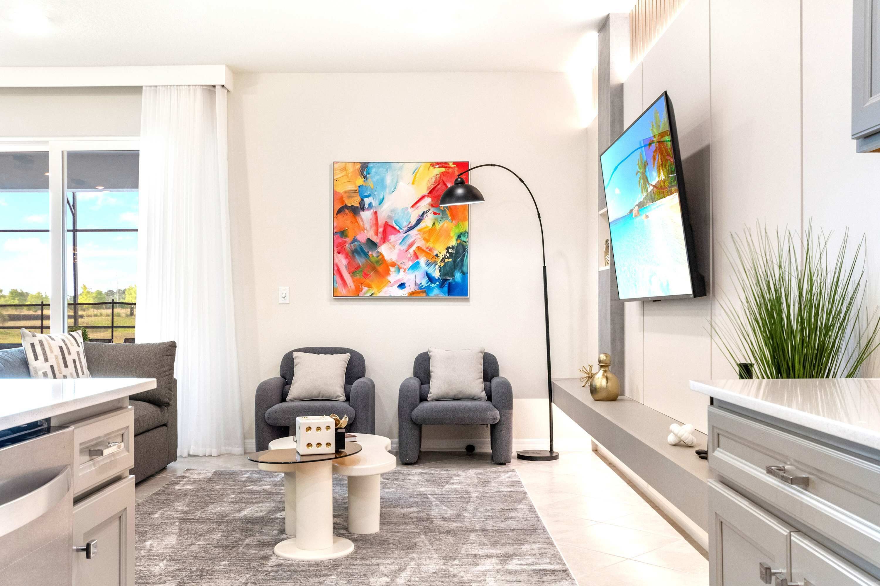 Una sala de estar moderna con un sofá gris, una mesa de centro, un televisor montado en la pared y un cuadro abstracto grande.