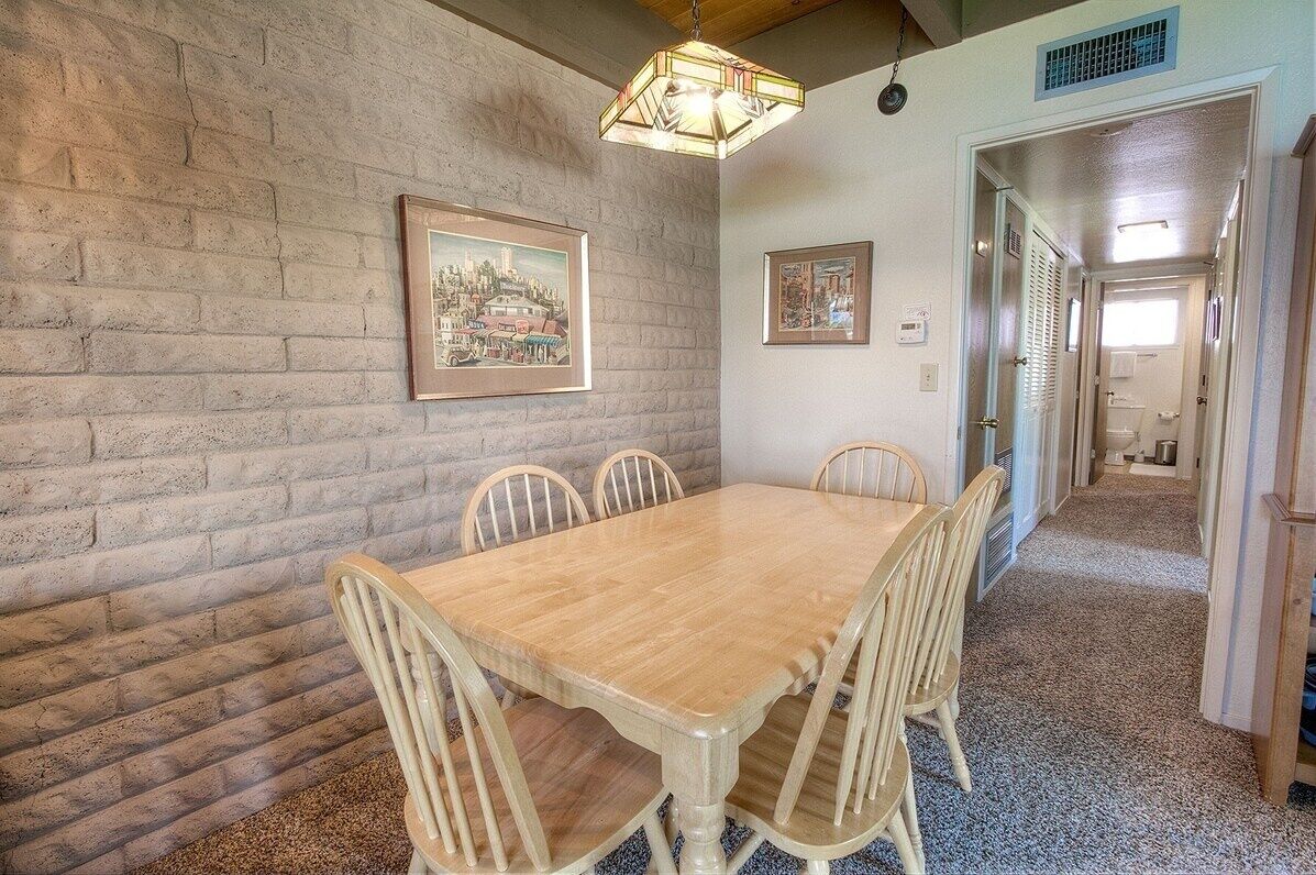 Un comedor con una mesa y sillas de madera, cuadros en la pared y un pasillo que conduce a otra habitación.