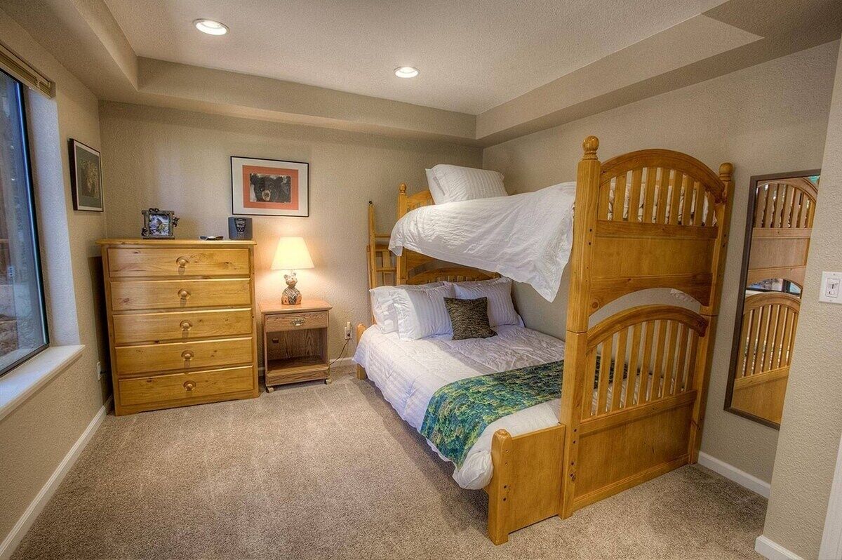 A bedroom with a bunk bed, a wooden dresser, a nightstand, and a lamp.