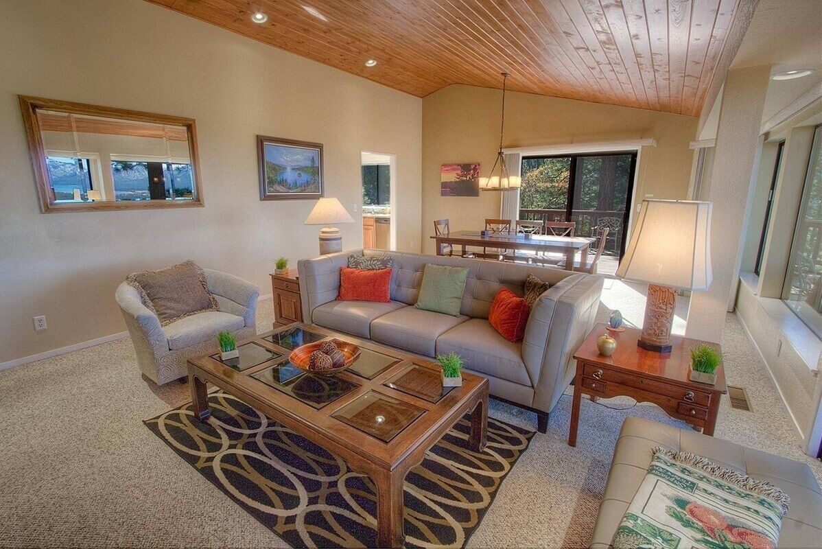 A spacious living room with a wooden ceiling, a glass coffee table, and a view of the outdoors.