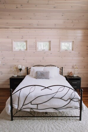 Un dormitorio con cama, dos mesitas de noche y tres ventanas.