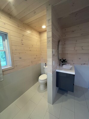Un baño con paredes de madera, un inodoro, un lavabo y una ventana.