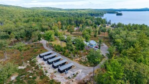 Luchtbeeld van een chaletgebied met meerdere chalets, een centraal gebouw en een meer op de achtergrond.