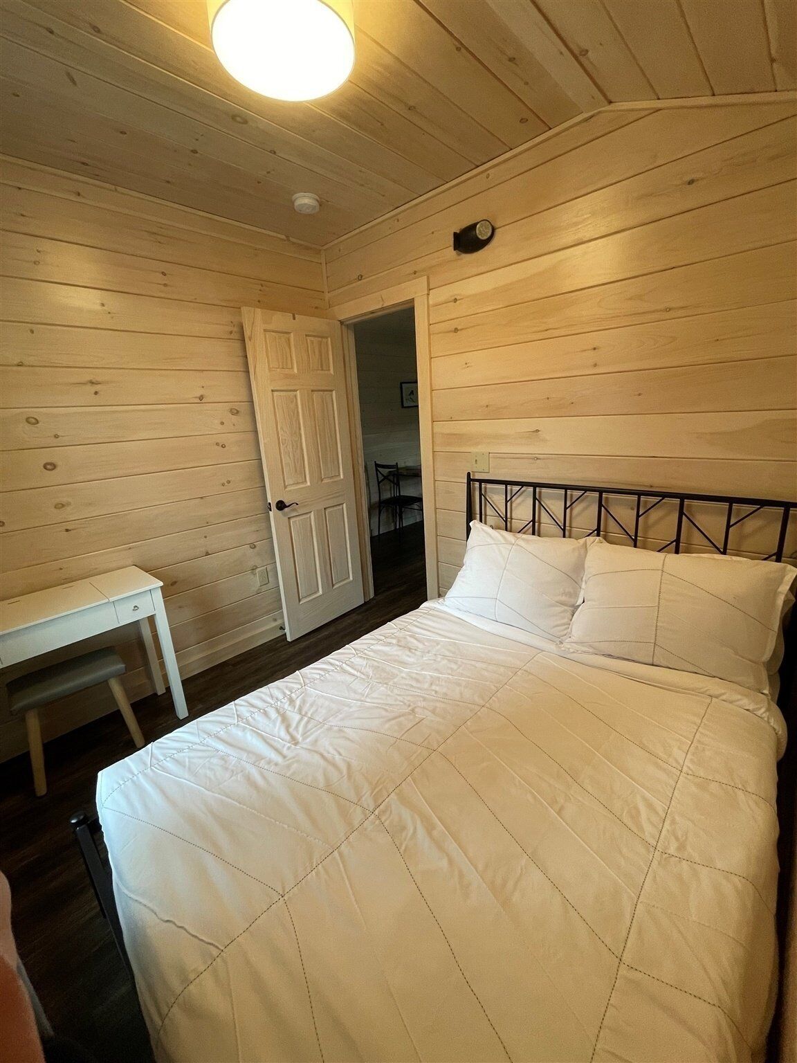 A bedroom with a bed, a desk, and a door leading to another room.