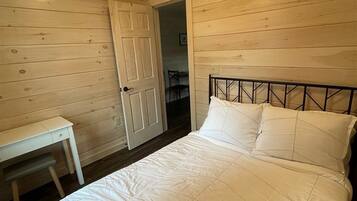 A bedroom with a bed, a desk, and a door leading to another room.