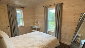 Une chambre à coucher dans un chalet en bois, avec un lit, une table de chevet, un miroir et une fenêtre avec des rideaux.