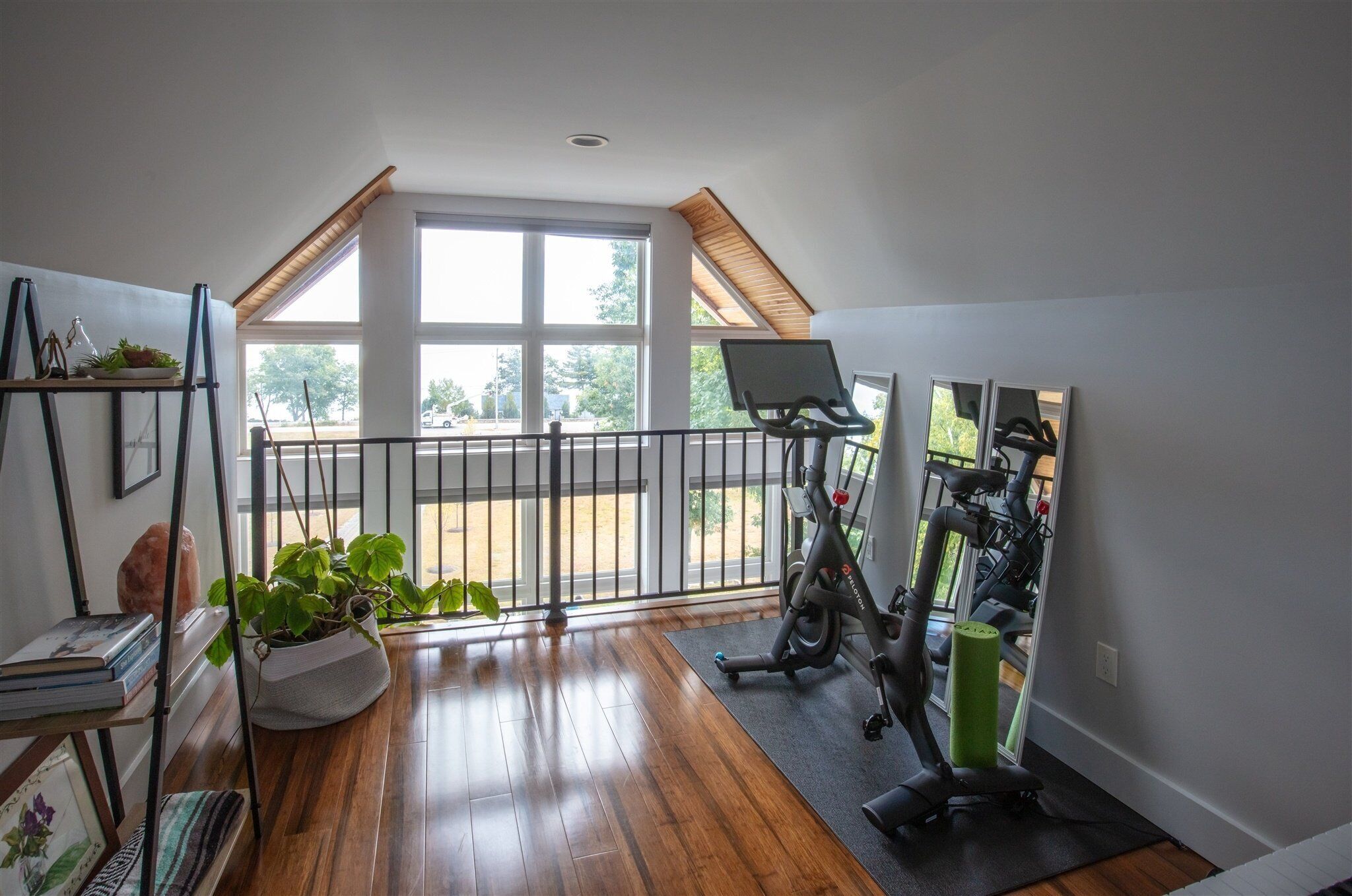 Une pièce spacieuse avec un plancher en bois, de grandes fenêtres, un balcon et un espace dédié à la salle de sport.