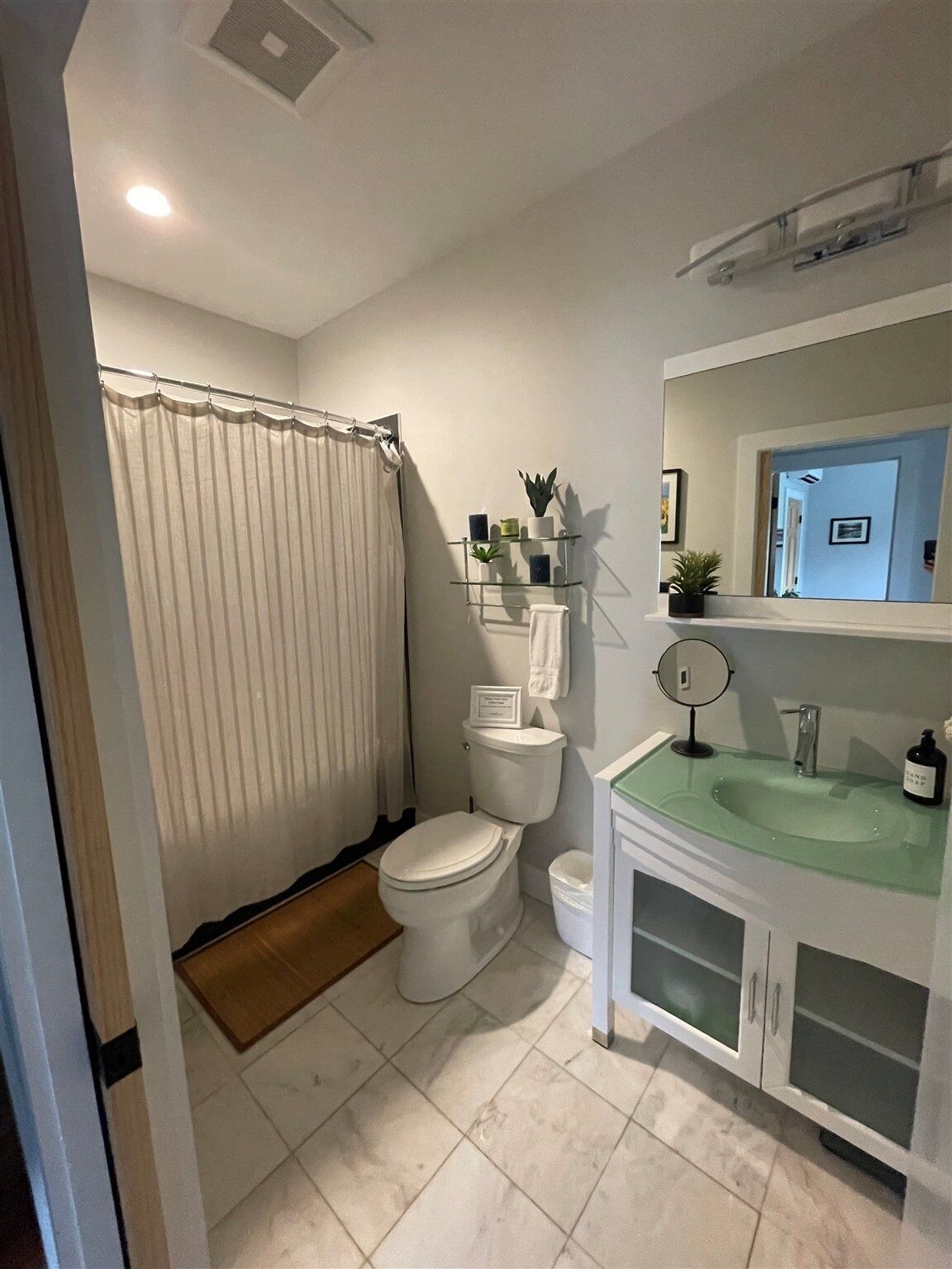 Une salle de bain équipée de toilettes, d’un lavabo en verre, d’un miroir et d’un rideau de douche.