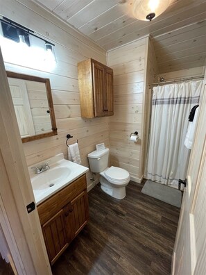 Un baño compacto con tocador de madera, inodoro y zona de ducha.