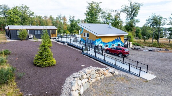A modern building with a colorful mural, a red car parked in front, and a gravel driveway. - Wood Thrush Limit 3 1 Bedroom Cabin (Sebago)