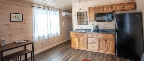 A compact kitchen with wooden cabinets, a black refrigerator, and a small dining area with a bench.