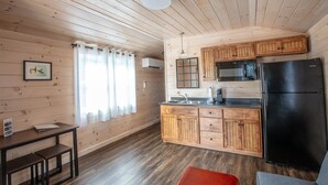 Eine kompakte Küche mit Holzausstattung, einem schwarzen Kühlschrank und einer kleinen Essecke mit einer Bank.
