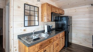 Eine Küche mit Holzausstattung, einem schwarzen Kühlschrank, einer Granitarbeitsplatte und einer Pendelleuchte.