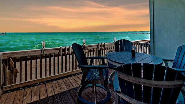 A wooden deck with a table and chairs overlooking the ocean at sunset. - Kontiki Bayfront 103 2 Bedroom Condo (Rockport)