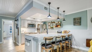 A modern kitchen with a large island, bar stools, and pendant lighting. - Kontiki Bayfront 103 2 Bedroom Condo (Rockport)