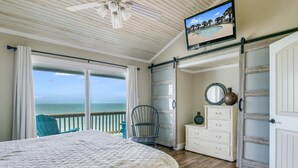 A bedroom with a large bed, a dresser, a chair, and a TV on the wall. - Kontiki Bayfront 103 2 Bedroom Condo (Rockport)