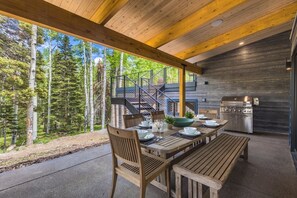 An outdoor dining area with a wooden table and chairs, a grill, and a view of a forested area. - Saddle Horn Lane 4 Bedroom Home (Telluride)