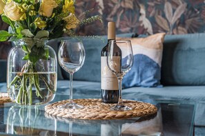 Een glazen tafel met een geweven tafelmat, een fles wijn, twee wijnglazen en een vaas met bloemen.