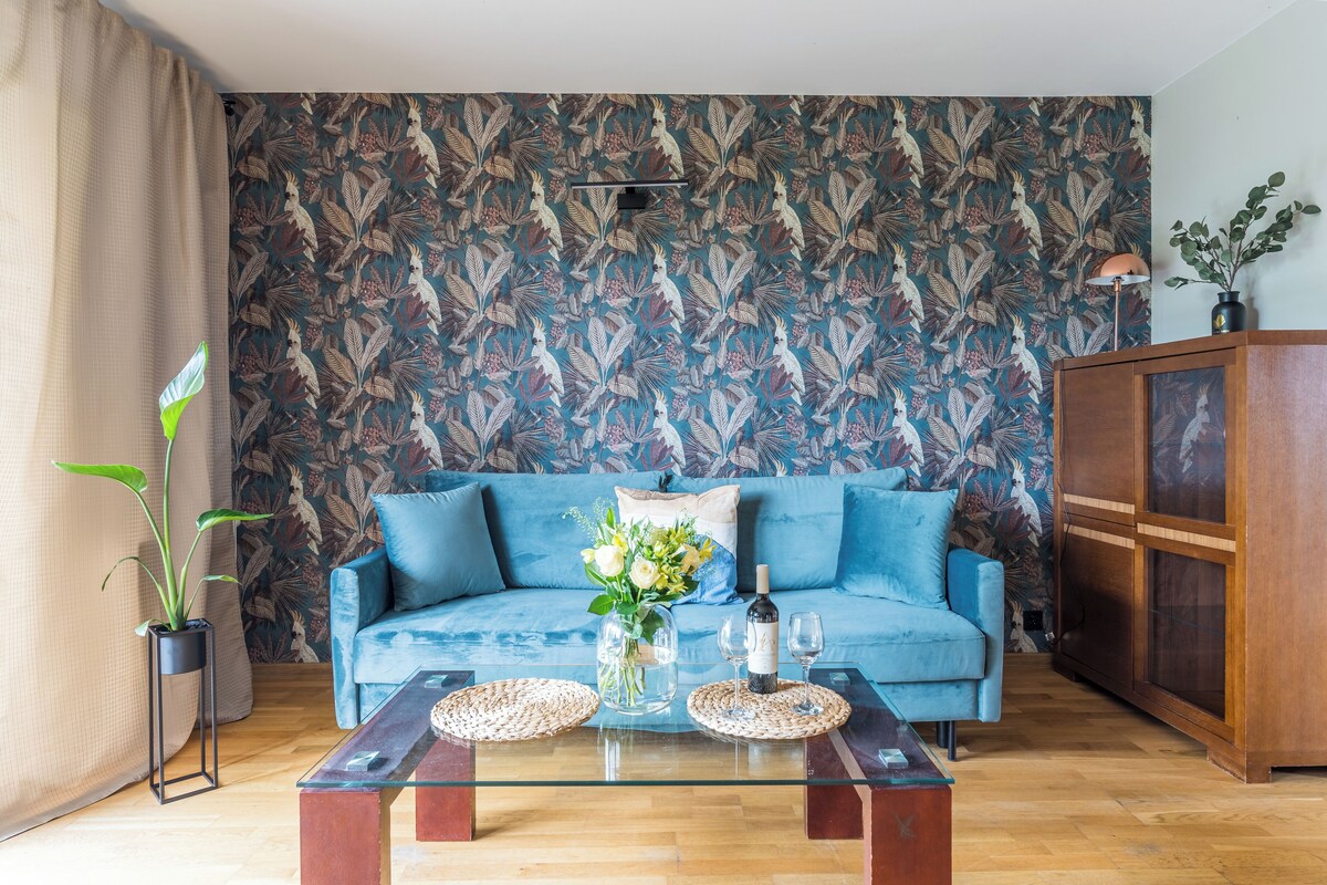 Un salon avec un canapé bleu, une table basse en verre, une plante en pot et un papier peint à motifs.