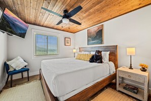 Ein Schlafzimmer mit Holzboden, einem Bett mit weißer Bettwäsche, einem blauen Sessel, einem Nachttisch mit Lampe und einem Gemälde an der Wand.