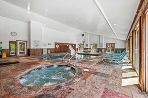 Un área de piscina interior con un jacuzzi, sillones de descanso y un cartel con las normas de la piscina.