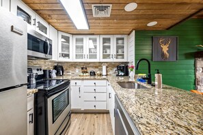 Eine moderne Küche mit weißen Schränken, Granit-Arbeitsplatten, einem Edelstahl-Kühlschrank und einer Wand in Grünton.