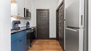 A narrow kitchen with blue cabinets, a stainless steel refrigerator, and a microwave. - Local Discounts!-The Revitalized Newark Arcade (Newark)