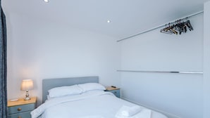 A hotel room with a bed, a nightstand with a lamp, a dresser, and a wall-mounted towel rack. - Cosy 1BR Apt in Manchester with Free Parking (Manchester)