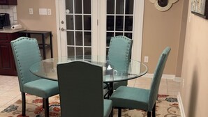 A dining area with a glass table and four upholstered chairs, a chandelier, a decorative mirror, and a floral-patterned rug. - “Welcome to this charming 3bedroom home in a quiet cul-de-sac in Evans Ga. (Evans)