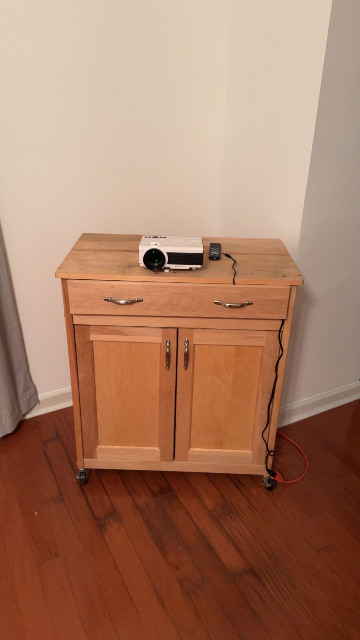 Un mueble de madera con dos cajones y un estante superior, un proyector en el estante y un control remoto.