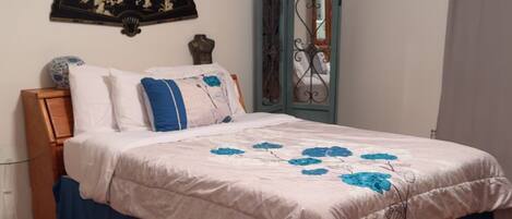 A bedroom with a bed, a ceiling fan, a decorative wall piece, a mirror, and a rug.