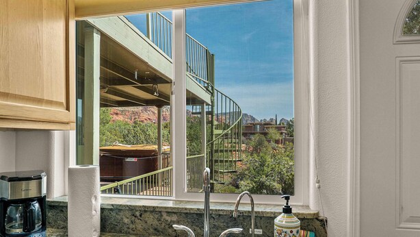 Una cocina con un lavamanos, una cafetera y una ventana con vista a una escalera en espiral y formaciones rocosas rojas.