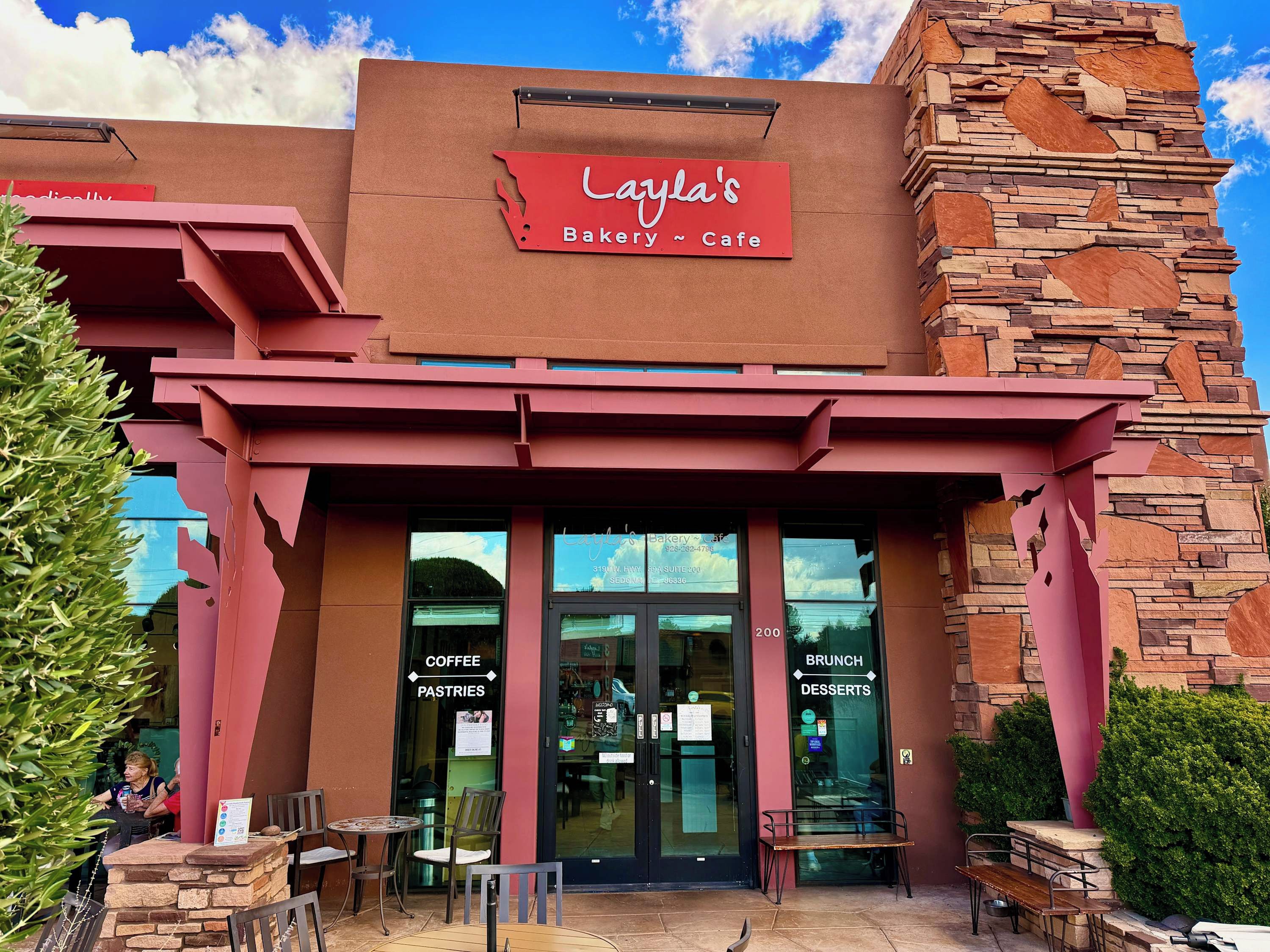 A bakery cafe with a stone facade, outdoor seating, and clear signage indicating coffee, pastries, and desserts.